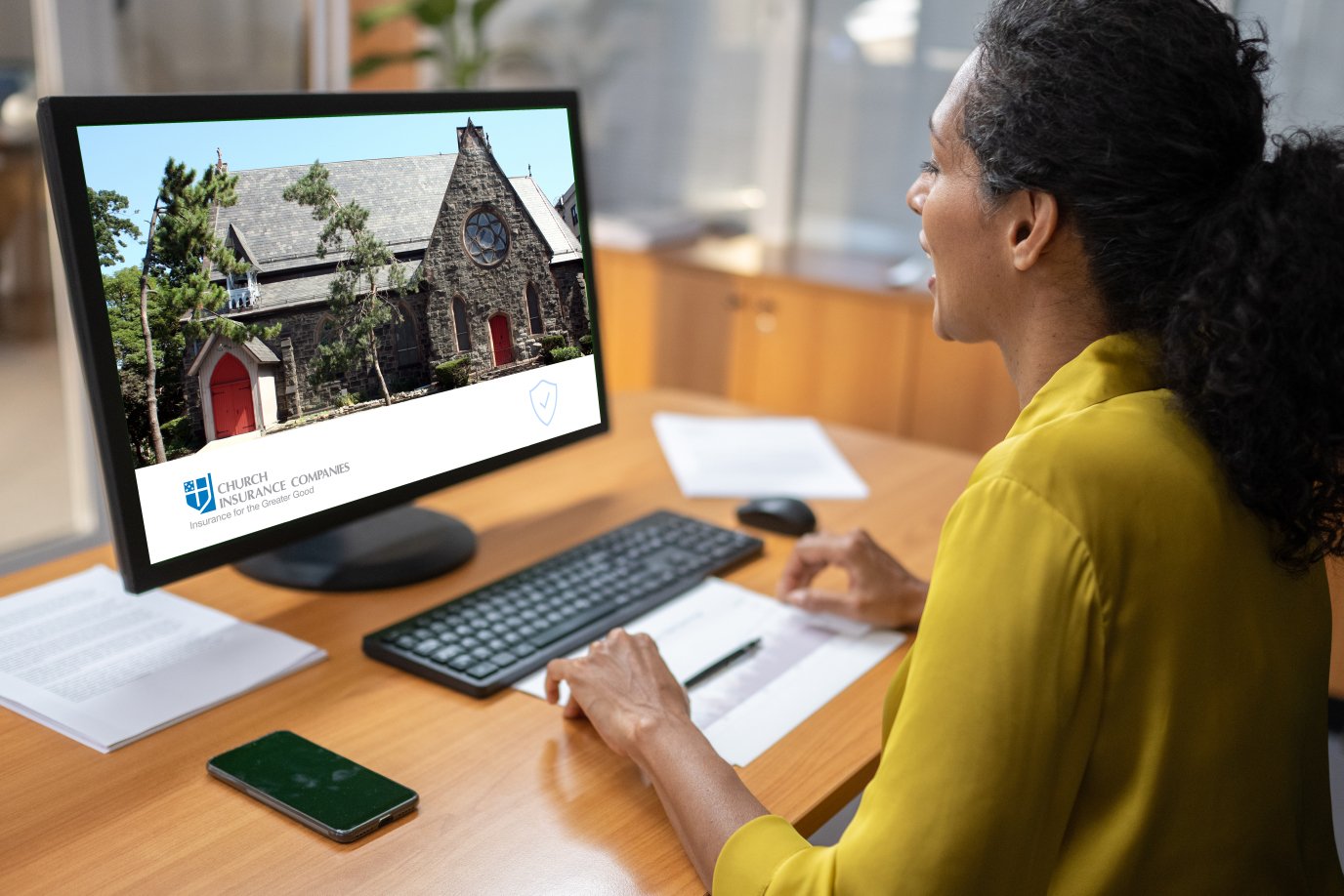 a woman with a yellow shirt is talking and looking at her screen. The screen has the CPG logo with a church buiding on it.